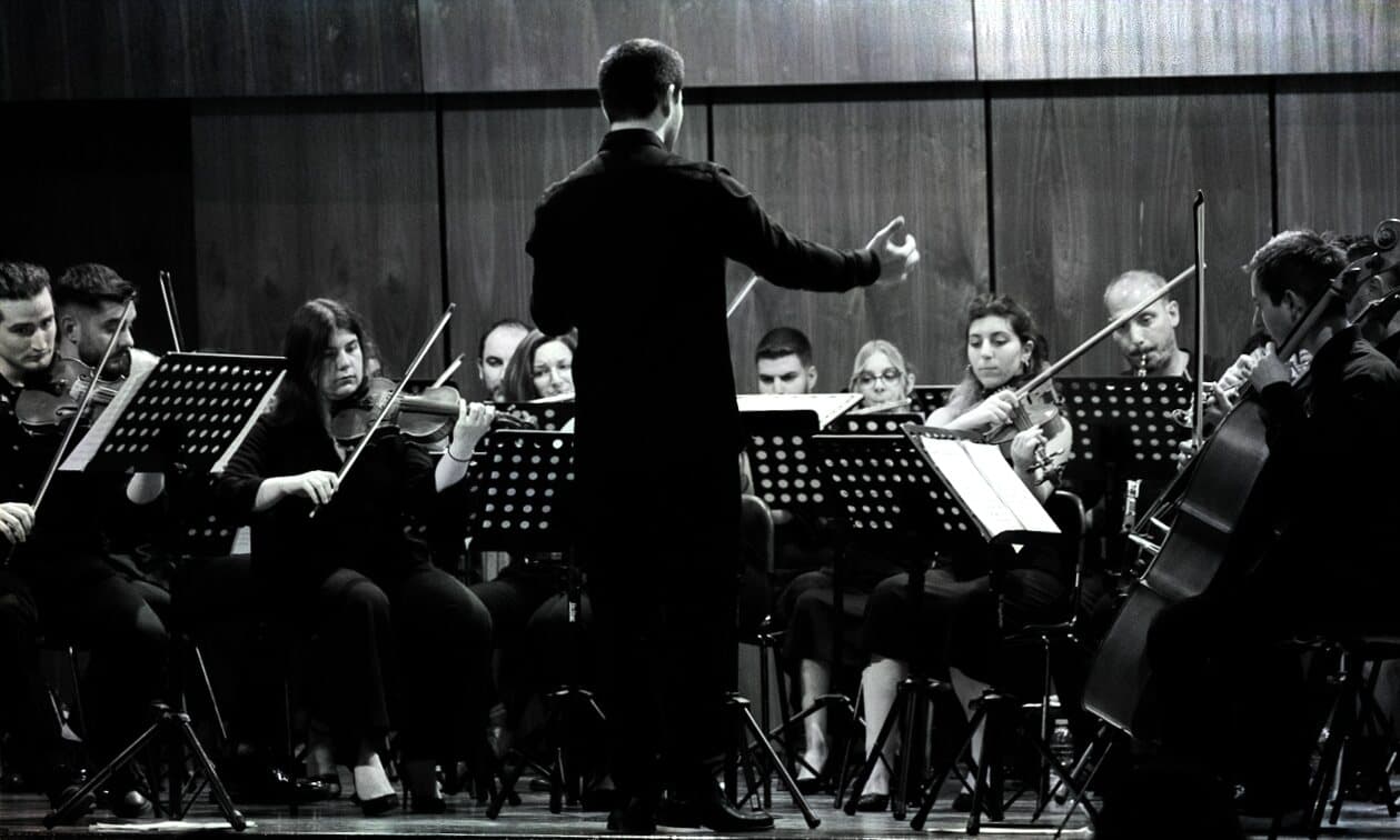 Vaggelis Stavropoulos conducting an orchestra on stage, black and white